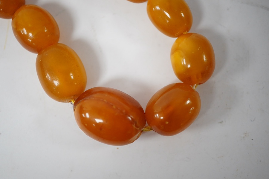 A single strand graduated oval amber bead necklace (a.f.), 90cm, gross weight 72 grams and three odd beads and an earring. Condition - poor